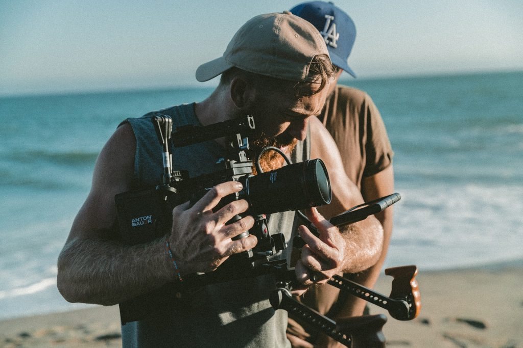 Hombre filmando en la playa con cámara profesional.