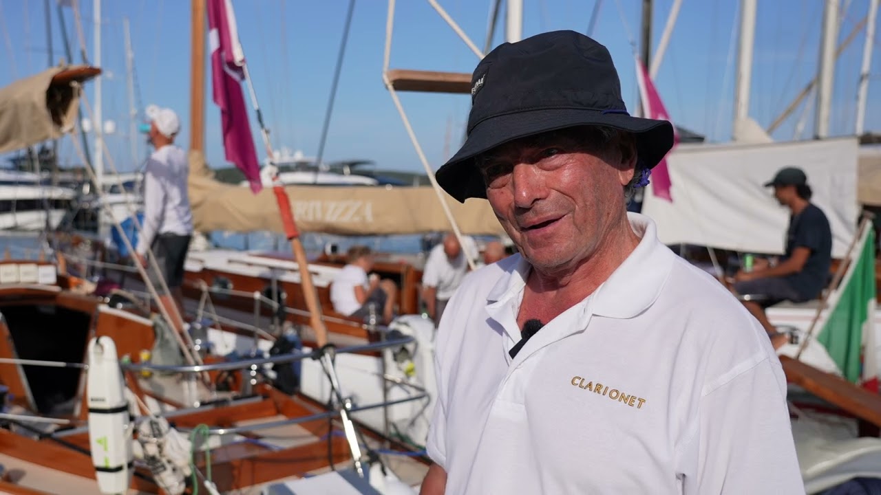 Hombre sonriente en un puerto con barcos.